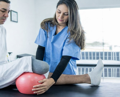 Physical therapist assisting a below-knee amputee with prosthetic rehabilitation exercises to improve strength, balance, and prosthetic success