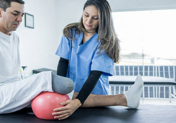 Physical therapist assisting a below-knee amputee with prosthetic rehabilitation exercises to improve strength, balance, and prosthetic success