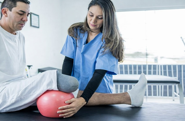 Physical therapist assisting a below-knee amputee with prosthetic rehabilitation exercises to improve strength, balance, and prosthetic success